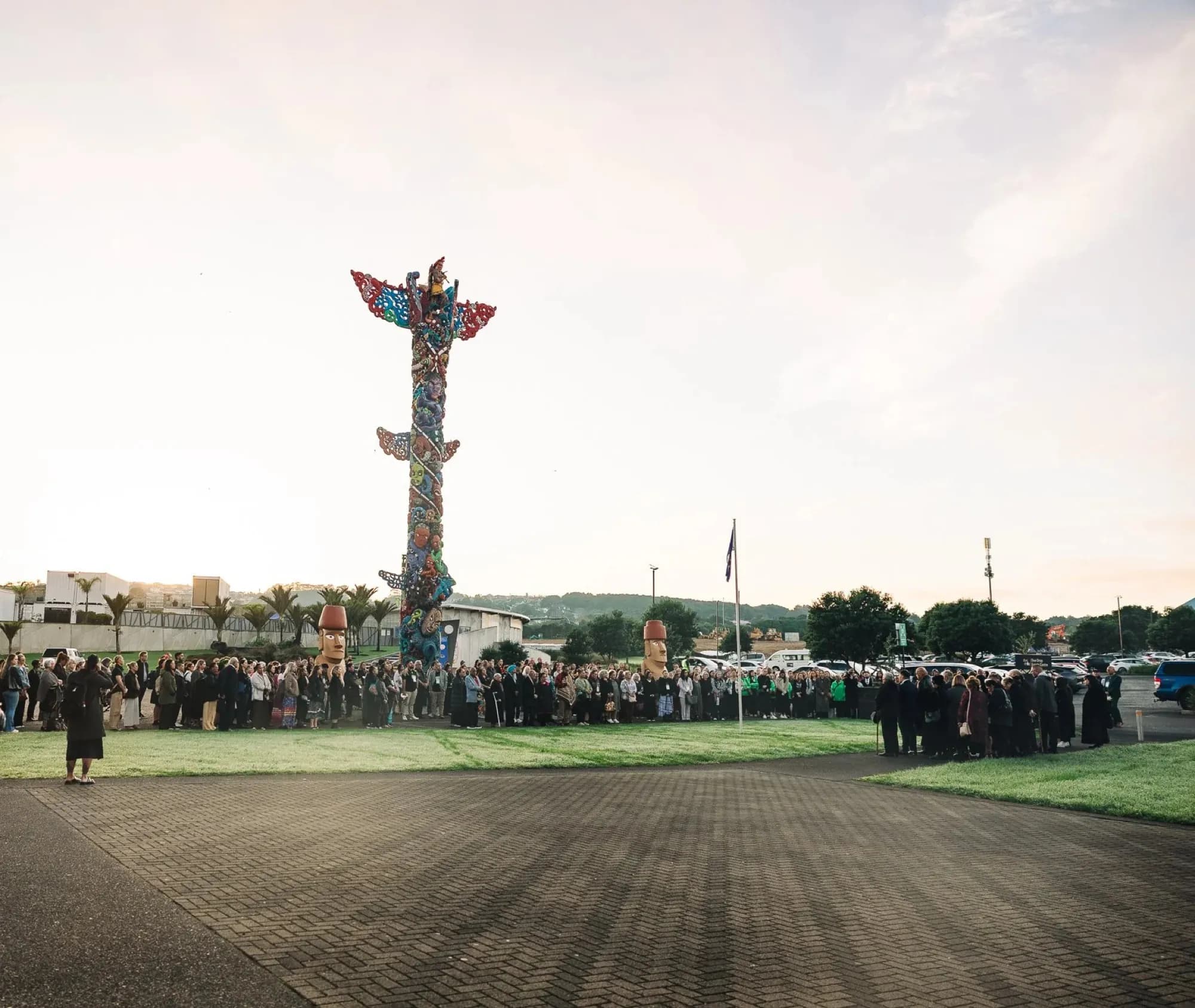 Manuhiri waiting on the grass at Pou Kapua at first light, before the pōwhiri that opened the World Indigenous Cancer Conference, Manukau, April 2026