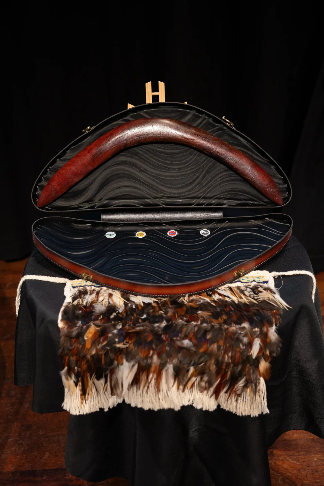 A carved taonga in a fitted case, resting on a feather cloak on the stage at the World Indigenous Cancer Conference, Tāmaki Makaurau, April 2026